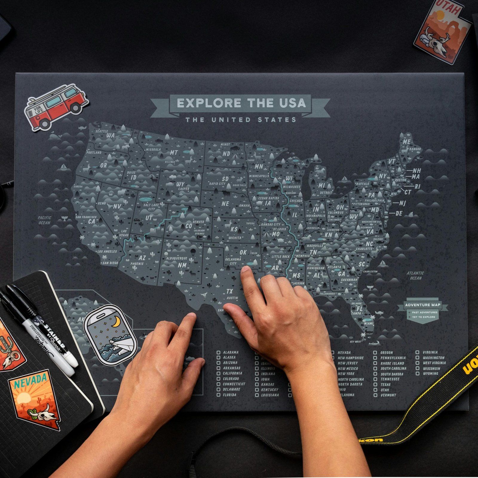Hands interacting with a USA map alongside travel essentials including a notebook and camera.